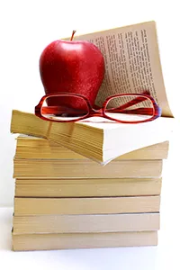 A stack of perfect bound books. The top one is open and has reading glasses and an apple sitting on it.